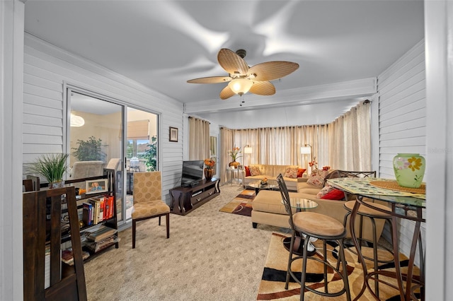 carpeted living room with ceiling fan and wood walls