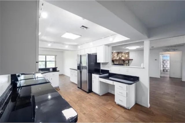 kitchen featuring stainless steel fridge, white cabinetry, hardwood / wood-style floors, and black stove