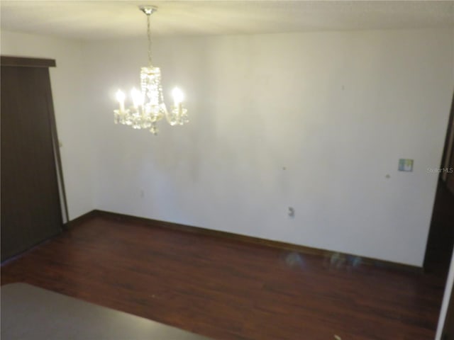 empty room with an inviting chandelier and dark wood-type flooring