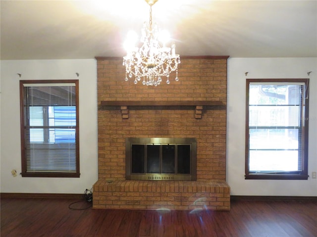 unfurnished living room featuring a notable chandelier, dark hardwood / wood-style floors, and a brick fireplace