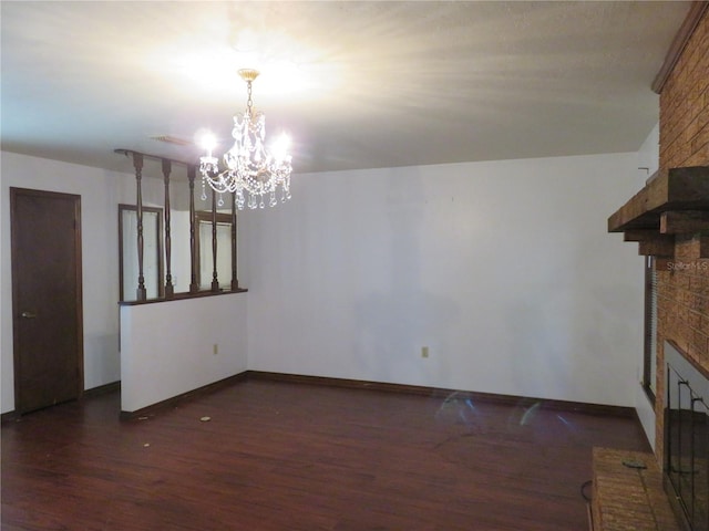 unfurnished living room with dark hardwood / wood-style floors, a brick fireplace, and a notable chandelier