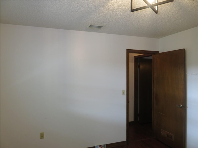 spare room featuring a textured ceiling and dark wood-type flooring