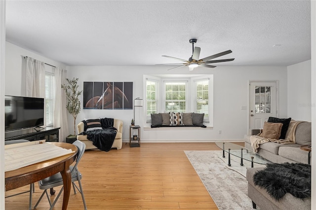 living room featuring plenty of natural light, ceiling fan, light wood-type flooring, and a textured ceiling