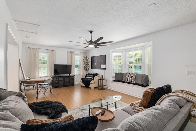 living room with ceiling fan, a textured ceiling, and light hardwood / wood-style floors