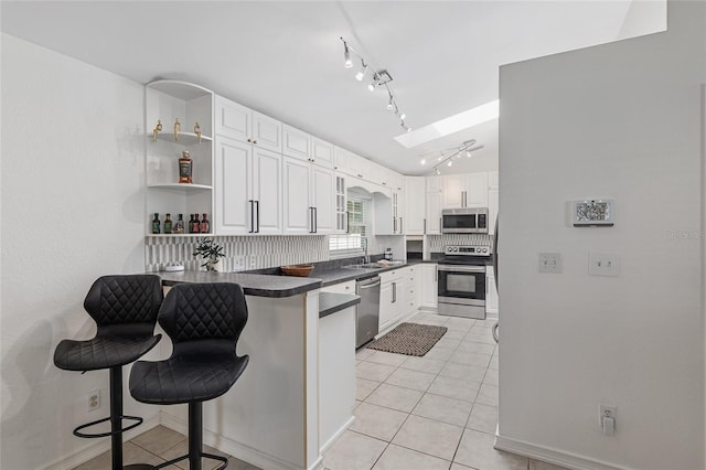 kitchen with a skylight, kitchen peninsula, white cabinetry, a breakfast bar area, and appliances with stainless steel finishes