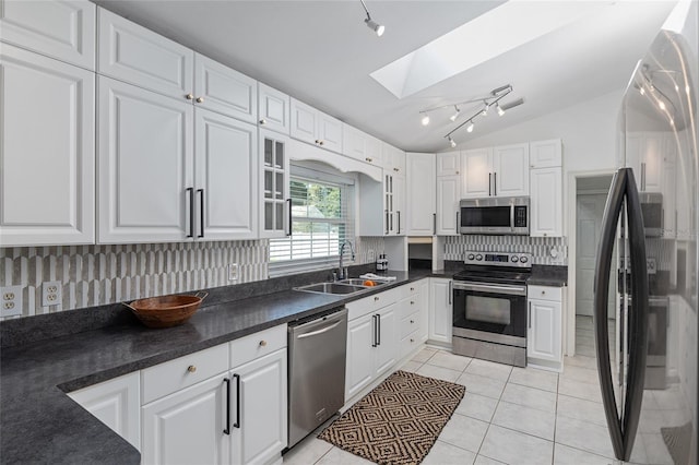 kitchen with lofted ceiling with skylight, stainless steel appliances, sink, and white cabinetry