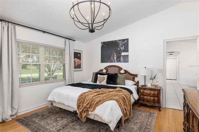 bedroom featuring a notable chandelier, vaulted ceiling, and light hardwood / wood-style floors