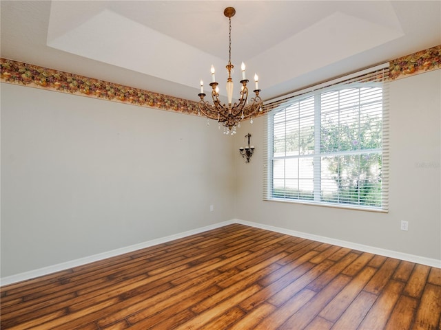 spare room featuring a notable chandelier, wood-type flooring, and a tray ceiling