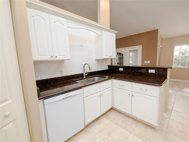 kitchen featuring white dishwasher, sink, backsplash, white cabinetry, and dark stone counters