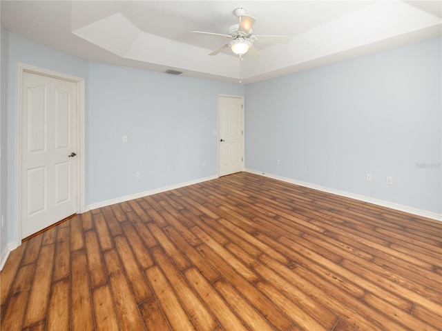 spare room featuring wood-type flooring, a tray ceiling, and ceiling fan