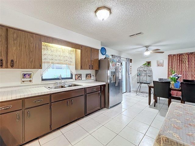 kitchen with light tile patterned floors, a textured ceiling, ceiling fan, stainless steel refrigerator with ice dispenser, and sink