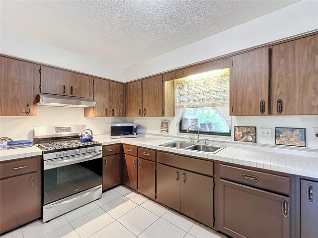 kitchen with a textured ceiling, tile counters, sink, stainless steel appliances, and light tile patterned floors