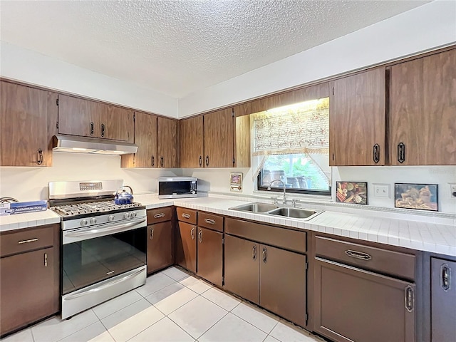 kitchen featuring a sink, appliances with stainless steel finishes, a textured ceiling, under cabinet range hood, and light tile patterned floors