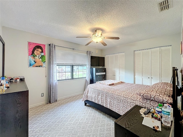 bedroom with light carpet, two closets, ceiling fan, and a textured ceiling