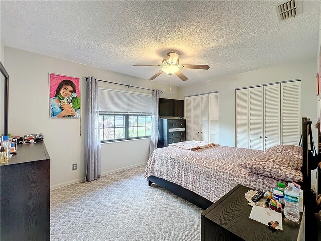 bedroom with carpet flooring, visible vents, two closets, baseboards, and ceiling fan