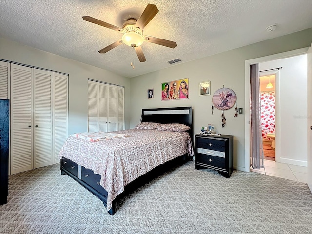 bedroom with multiple closets, ceiling fan, light colored carpet, and a textured ceiling