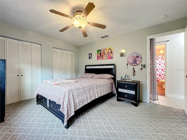 bedroom featuring two closets, a textured ceiling, carpet floors, ceiling fan, and visible vents