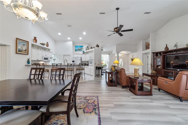 dining area with ceiling fan with notable chandelier, lofted ceiling, and light hardwood / wood-style floors