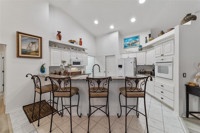 kitchen with a breakfast bar, dark stone counters, white cabinets, kitchen peninsula, and white appliances