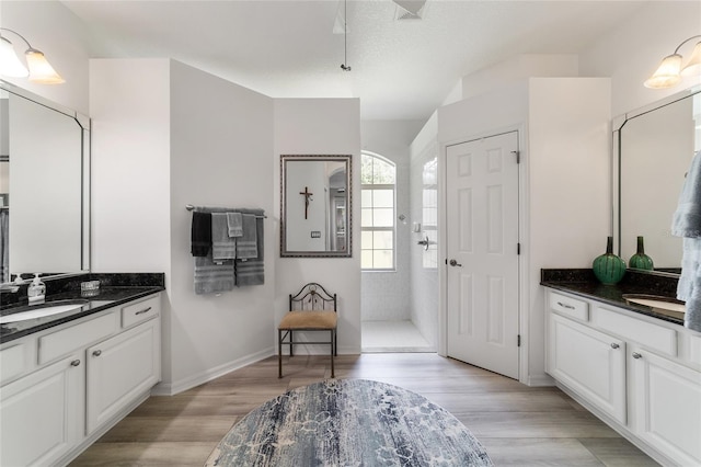 bathroom with a textured ceiling, hardwood / wood-style flooring, vanity, and tiled shower