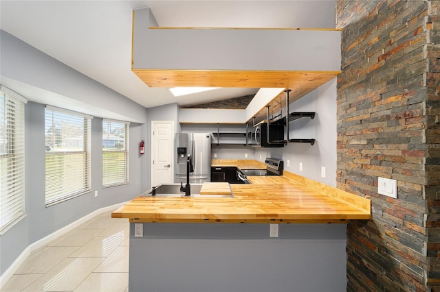 kitchen featuring kitchen peninsula, appliances with stainless steel finishes, wooden counters, a breakfast bar, and lofted ceiling