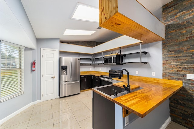 kitchen with butcher block countertops, kitchen peninsula, vaulted ceiling, a kitchen bar, and appliances with stainless steel finishes