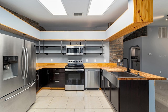 kitchen with kitchen peninsula, light tile patterned floors, stainless steel appliances, and butcher block counters