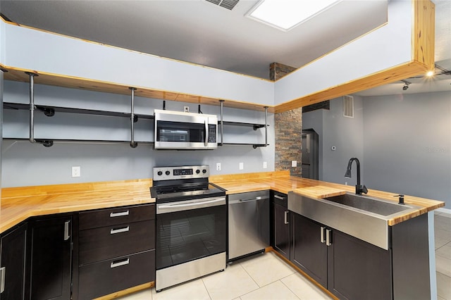 kitchen with kitchen peninsula, stainless steel appliances, sink, light tile patterned floors, and butcher block counters