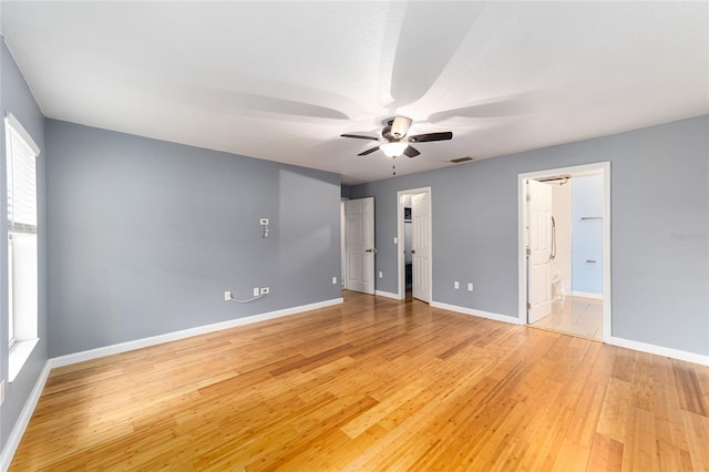 unfurnished bedroom with light wood-type flooring, a spacious closet, ensuite bath, and ceiling fan