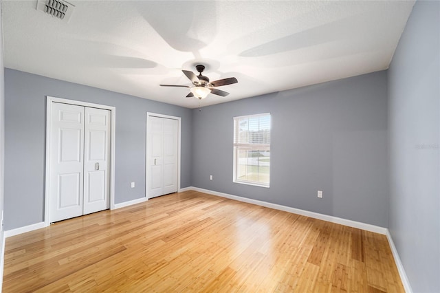 unfurnished bedroom with ceiling fan, wood-type flooring, a textured ceiling, and two closets