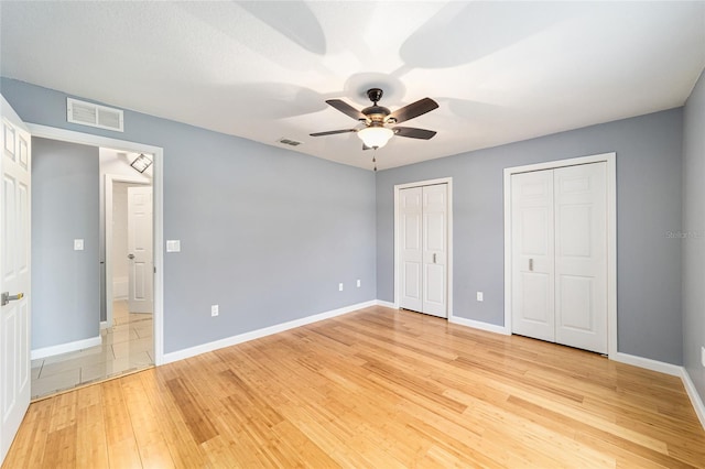 unfurnished bedroom featuring ceiling fan, light wood-type flooring, and multiple closets