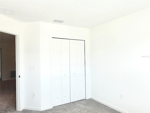 unfurnished bedroom with a textured ceiling, carpet flooring, and a closet