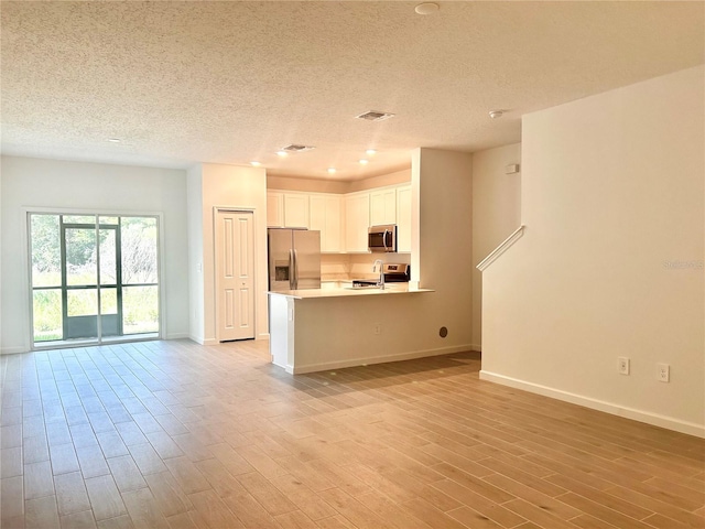 kitchen featuring appliances with stainless steel finishes, a textured ceiling, light hardwood / wood-style floors, and white cabinets