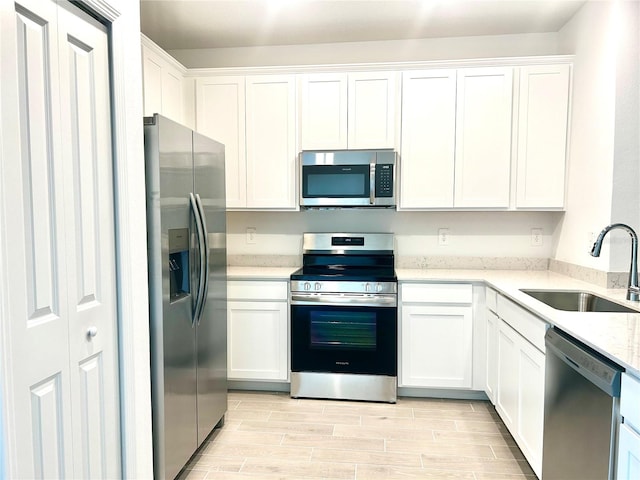 kitchen featuring light wood-type flooring, sink, white cabinets, appliances with stainless steel finishes, and light stone countertops