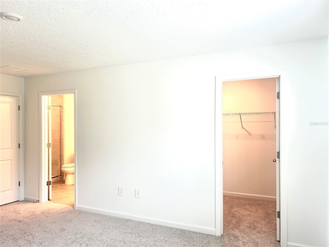 unfurnished bedroom with light colored carpet, a textured ceiling, ensuite bath, and a spacious closet