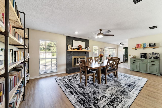 dining room with a textured ceiling, a fireplace, hardwood / wood-style flooring, and ceiling fan