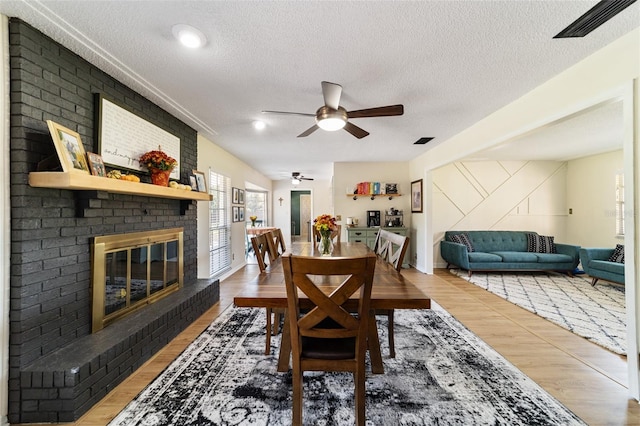 dining area with a textured ceiling, hardwood / wood-style flooring, ceiling fan, and a brick fireplace