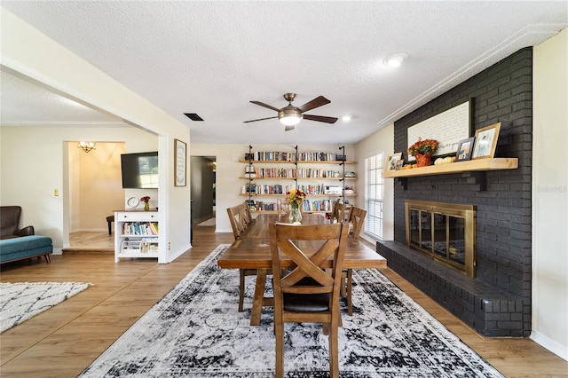 dining room featuring a textured ceiling, wood-type flooring, and a brick fireplace