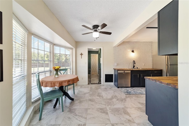 kitchen featuring sink, a textured ceiling, ceiling fan, stainless steel dishwasher, and wooden counters