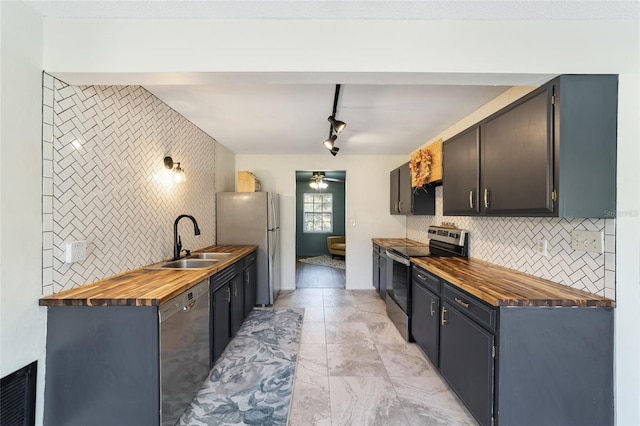 kitchen with butcher block counters, track lighting, stainless steel appliances, sink, and ceiling fan