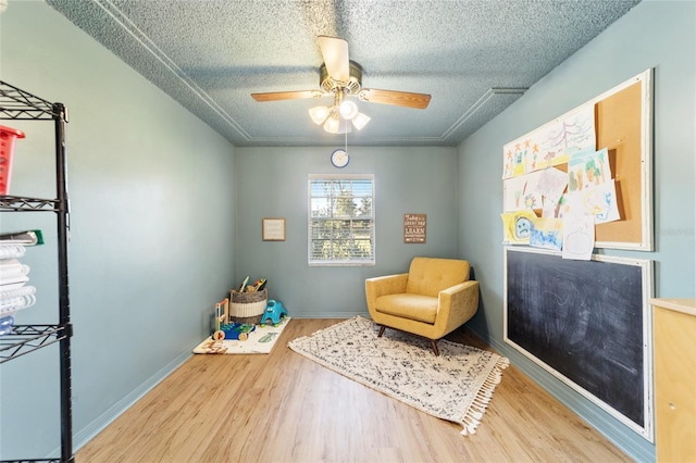 living area featuring ceiling fan, hardwood / wood-style flooring, and a textured ceiling