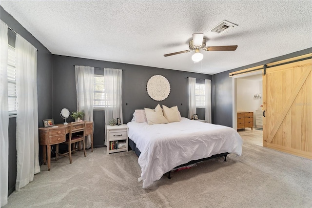 carpeted bedroom featuring connected bathroom, a barn door, multiple windows, and ceiling fan