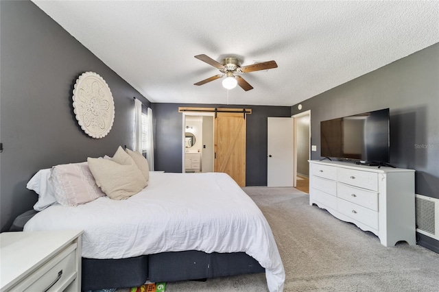 bedroom with connected bathroom, a barn door, light colored carpet, a textured ceiling, and ceiling fan