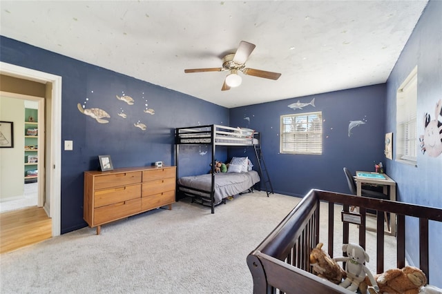 carpeted bedroom with a crib and ceiling fan