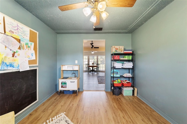 playroom featuring a ceiling fan, light wood-type flooring, a textured ceiling, and baseboards