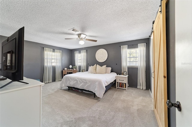 bedroom featuring visible vents, a barn door, a ceiling fan, light carpet, and a textured ceiling