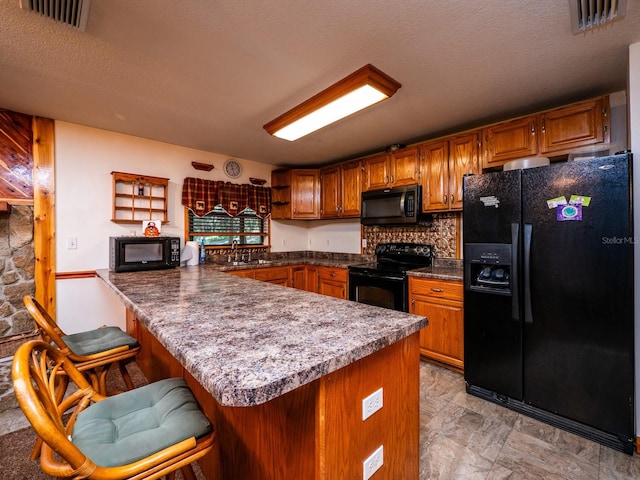 kitchen with a breakfast bar area, kitchen peninsula, a textured ceiling, and black appliances