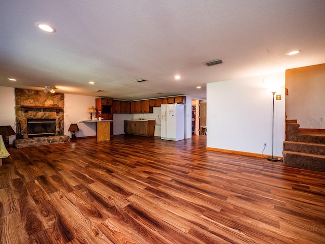 living room with a textured ceiling, a stone fireplace, and dark wood-type flooring