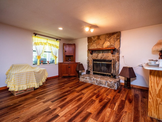 living room with a textured ceiling, a stone fireplace, and dark wood-type flooring