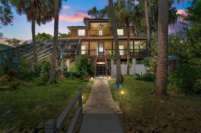 back house at dusk featuring a lawn, ceiling fan, and glass enclosure